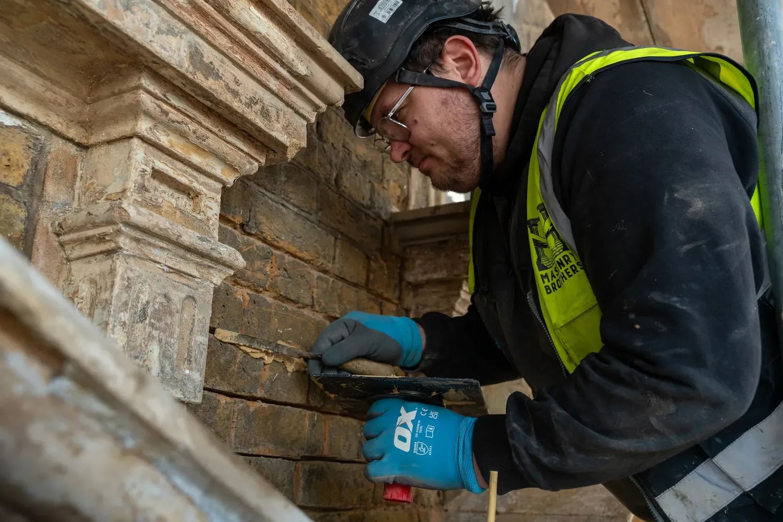 Skilled craftsman repointing traditional brickwork near a stone cornice