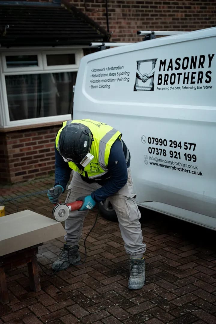Masonry Brothers worker shaping stone beside the branded company van